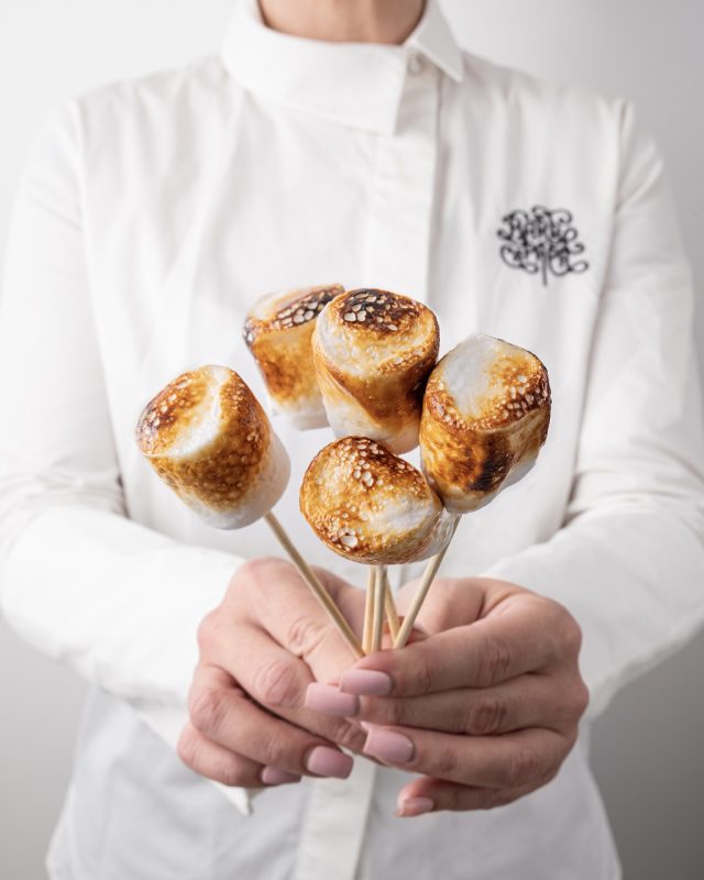 Bouquet gourmand de marshmallows dorés au feu, tenu par une barbista en chemise blanche