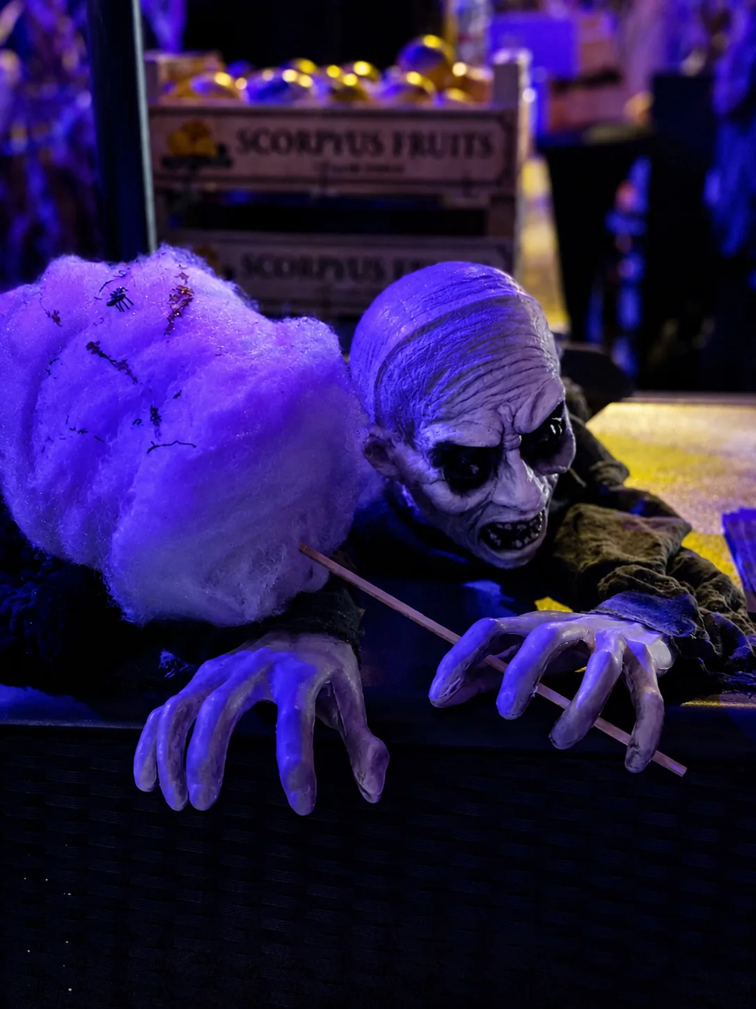Créature d'Halloween tendant la main vers une barbe à papa violette sous lumière noire