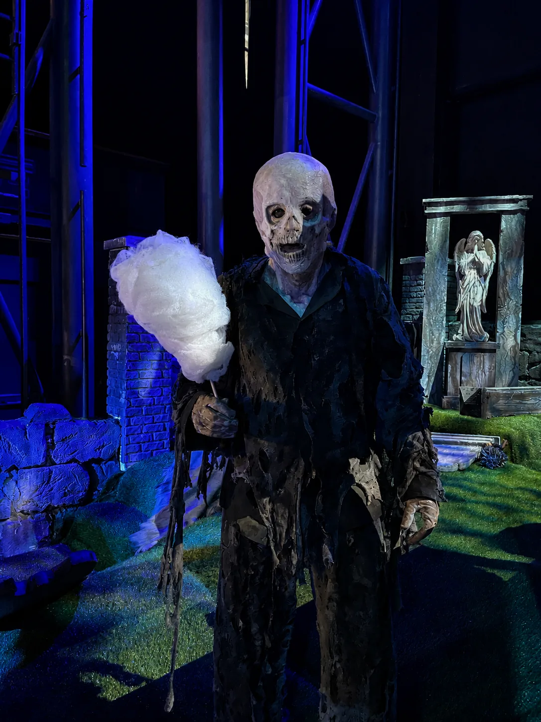 Zombie costumé tenant une barbe à papa d'Halloween dans un décor de cimetière
