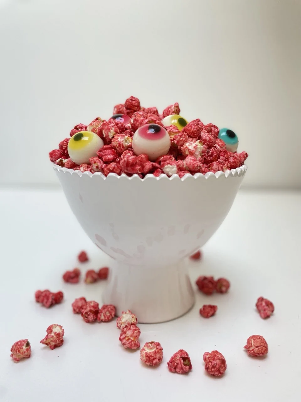 Pop-corn rouge d'Halloween garni de bonbons en forme d'yeux, servi dans une coupe blanche